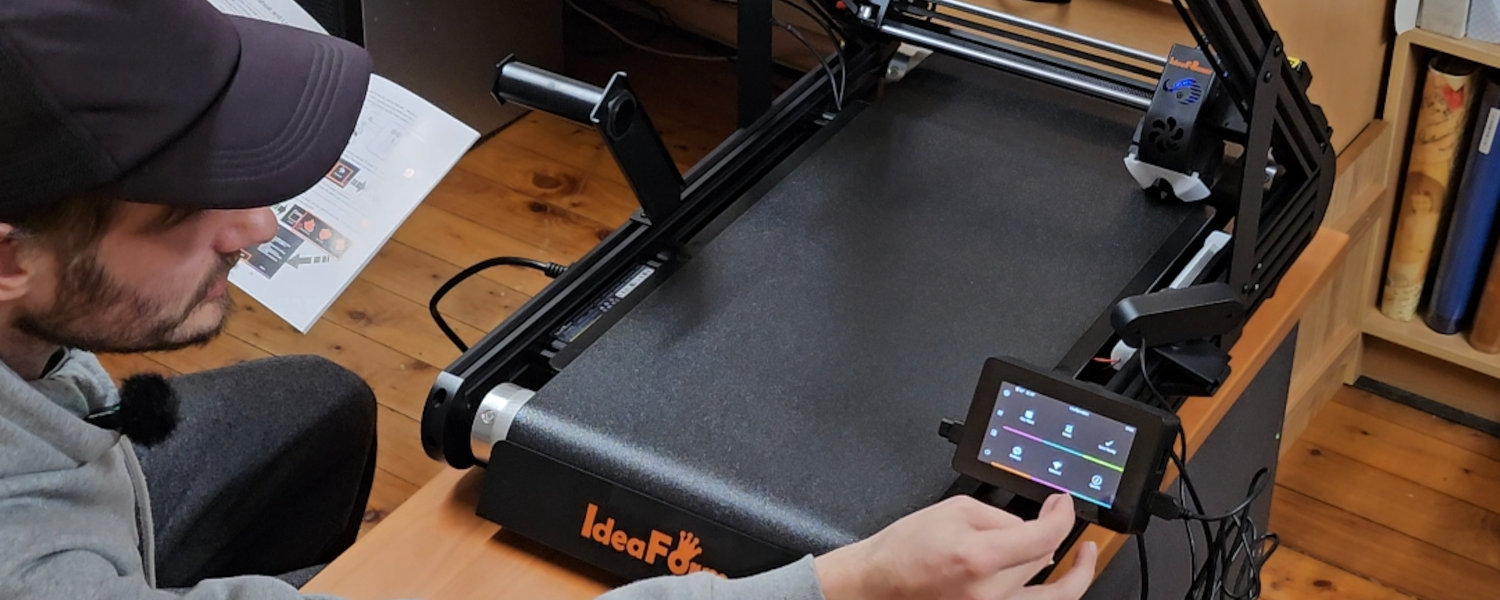 A man is engaged in 3D printing, carefully monitoring the process of producing a model in a modern workspace.