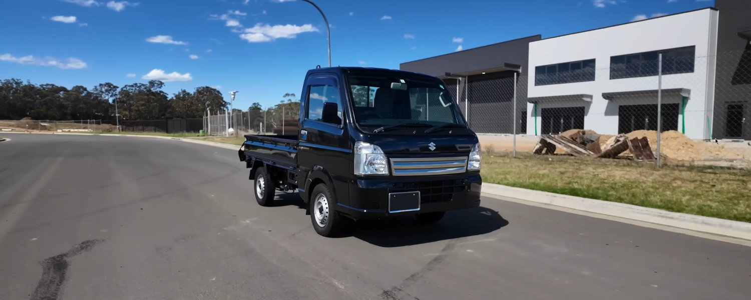 A small truck drives along the road in front of a building, showcasing urban transportation in action.
