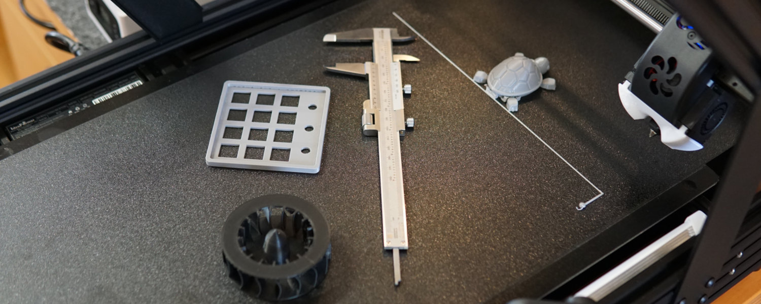 A 3D printer positioned next to a few 3d printed components and a ruler, illustrating tools for reverse engineering and measurement.